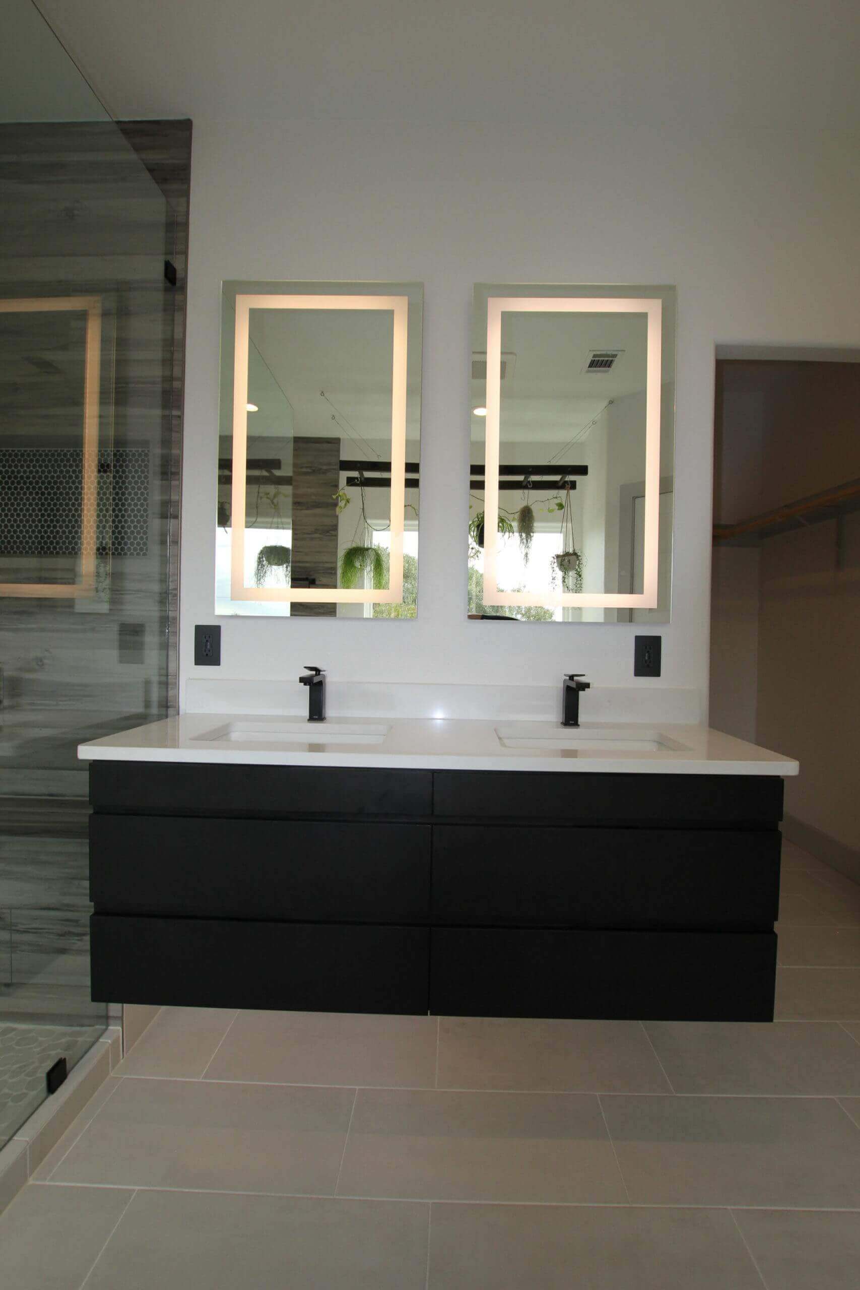 Floating black bathroom cabinets with double sinks and two LED lit vanity mirrors