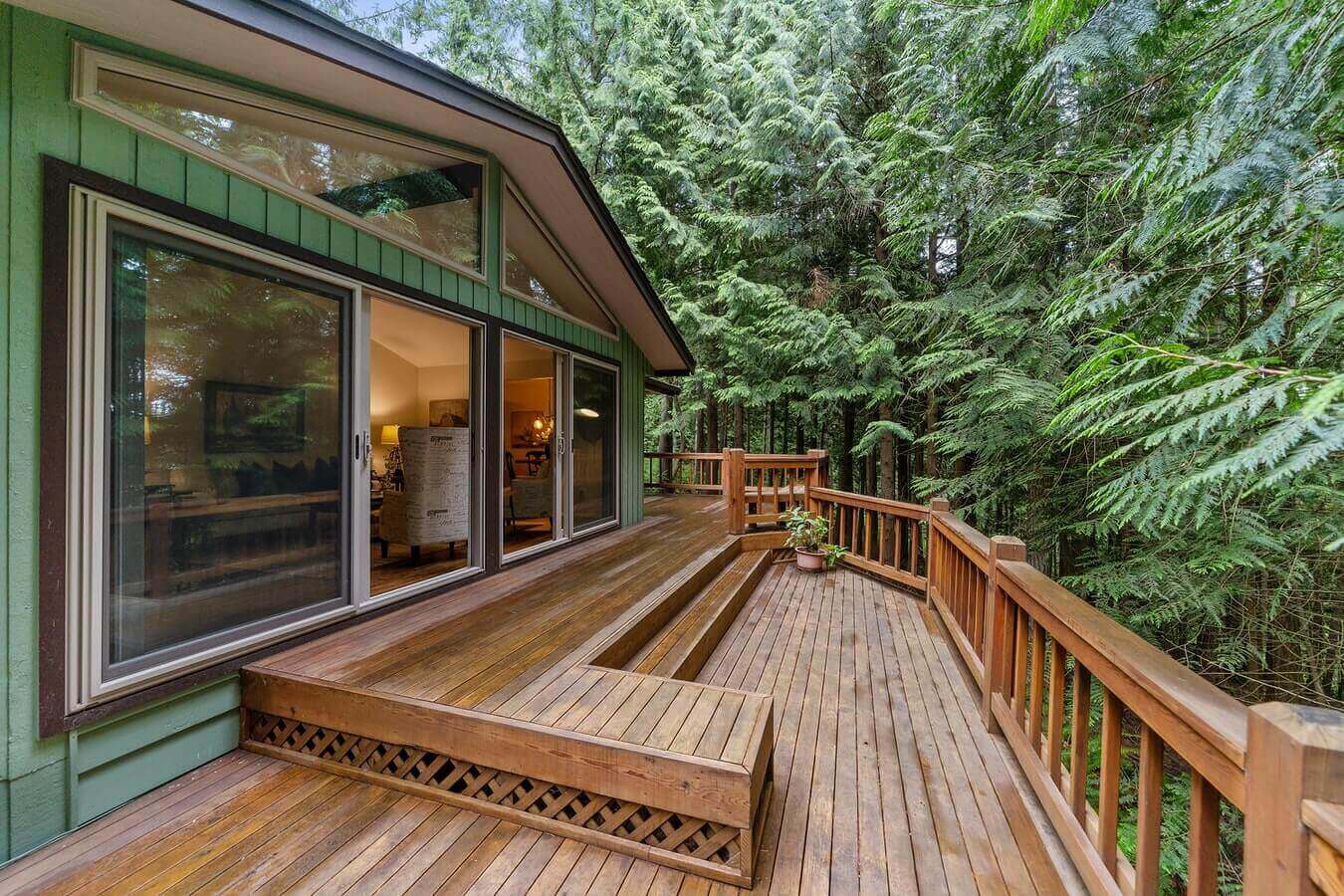 A large deck attached to a green house surrounded by pine trees