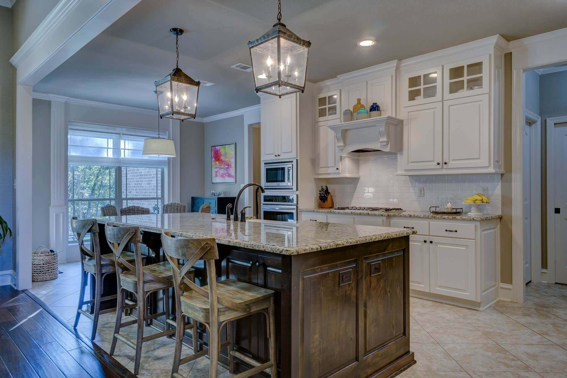 A southern styled kitchen with custom white cabinets, tan tiled floors, and an island bar in the middle