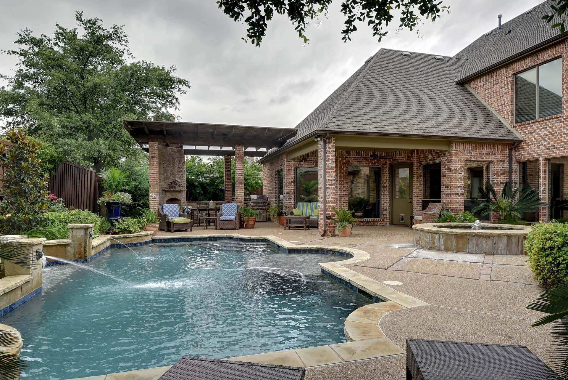 A luxurious pool with fountains next to a large brick home