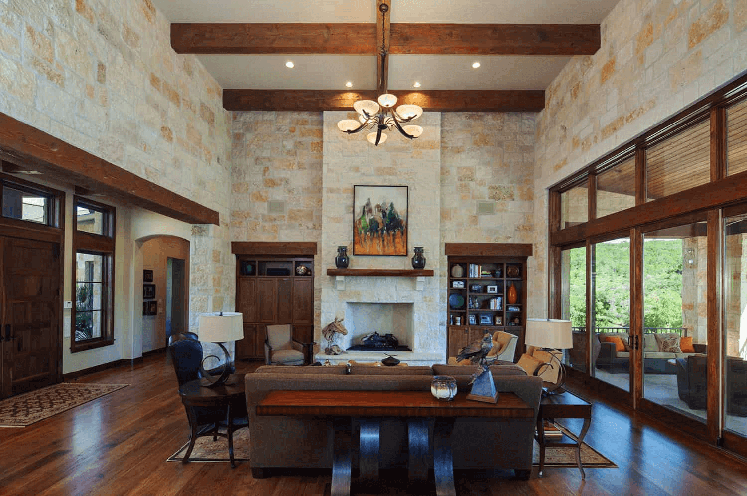 Home interior remodel with wood beams, wooden floors, large glass door opening onto a patio. Tall ceilings and stone walls