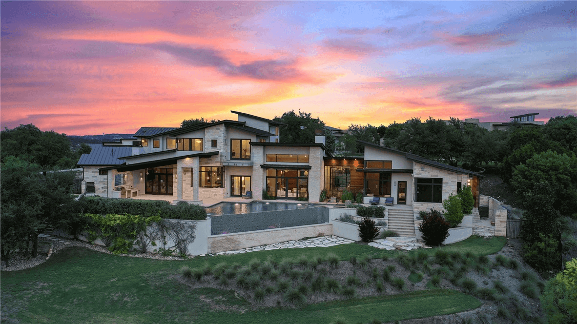 Custom home with tons of windows and white stone walls. An infinity pool looks out at a valley with a sunset in the background